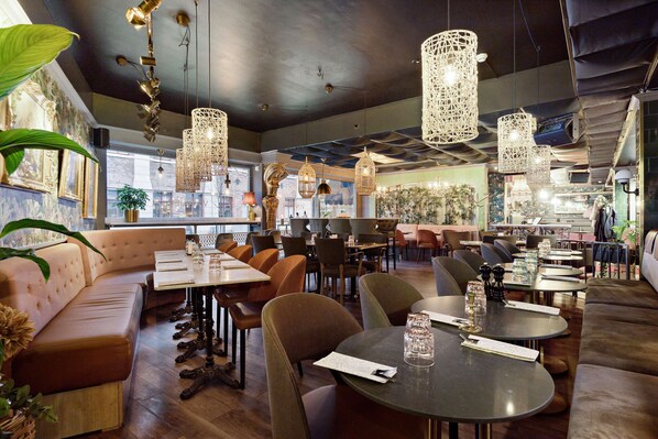 Un restaurante con mesas altas, asientos acolchados y lámparas colgantes.