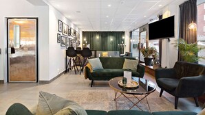 A modern hotel lobby with a green sofa, a round coffee table, and a flat-screen TV mounted on the wall. - Best Western Plaza Hotel (Eskilstuna)