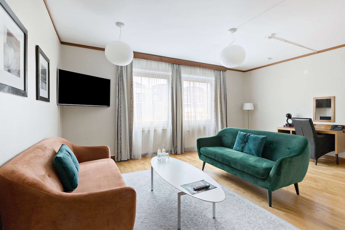Een moderne woonkamer met een bruine bank, een groene bank, een witte salontafel en een flatscreen televisie die aan de muur is bevestigd.