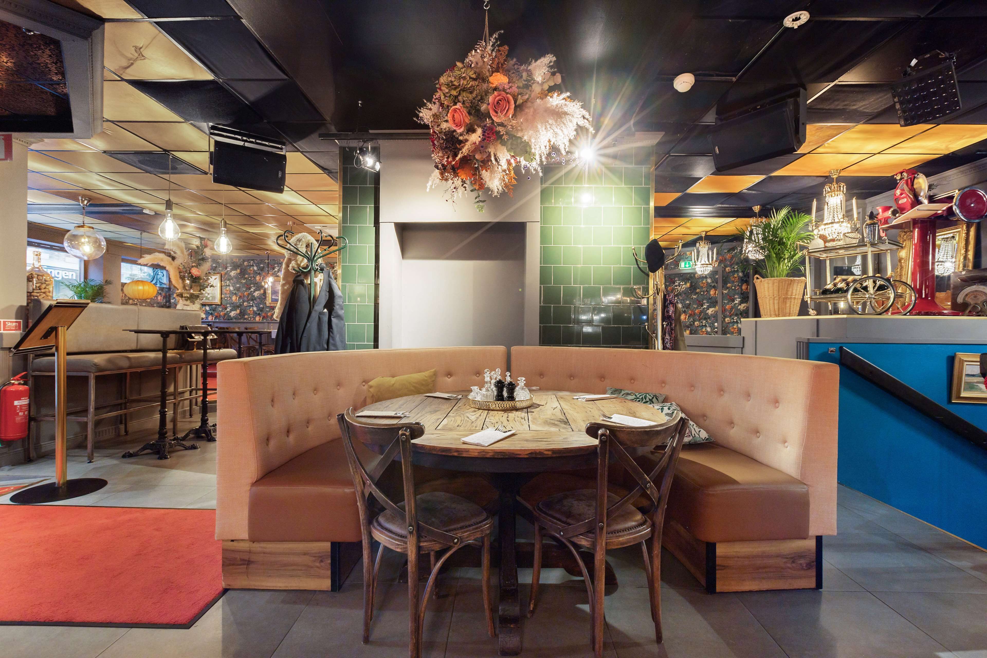 A cozy dining area with a round table, cushioned seating, and a hanging floral centerpiece.