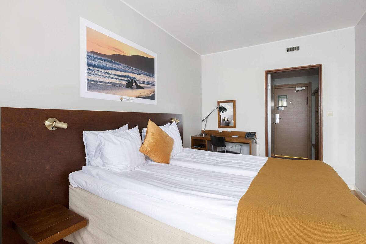 Een hotelkamer met een groot bed, een bureau met stoel, een nachtkastje en een deur.