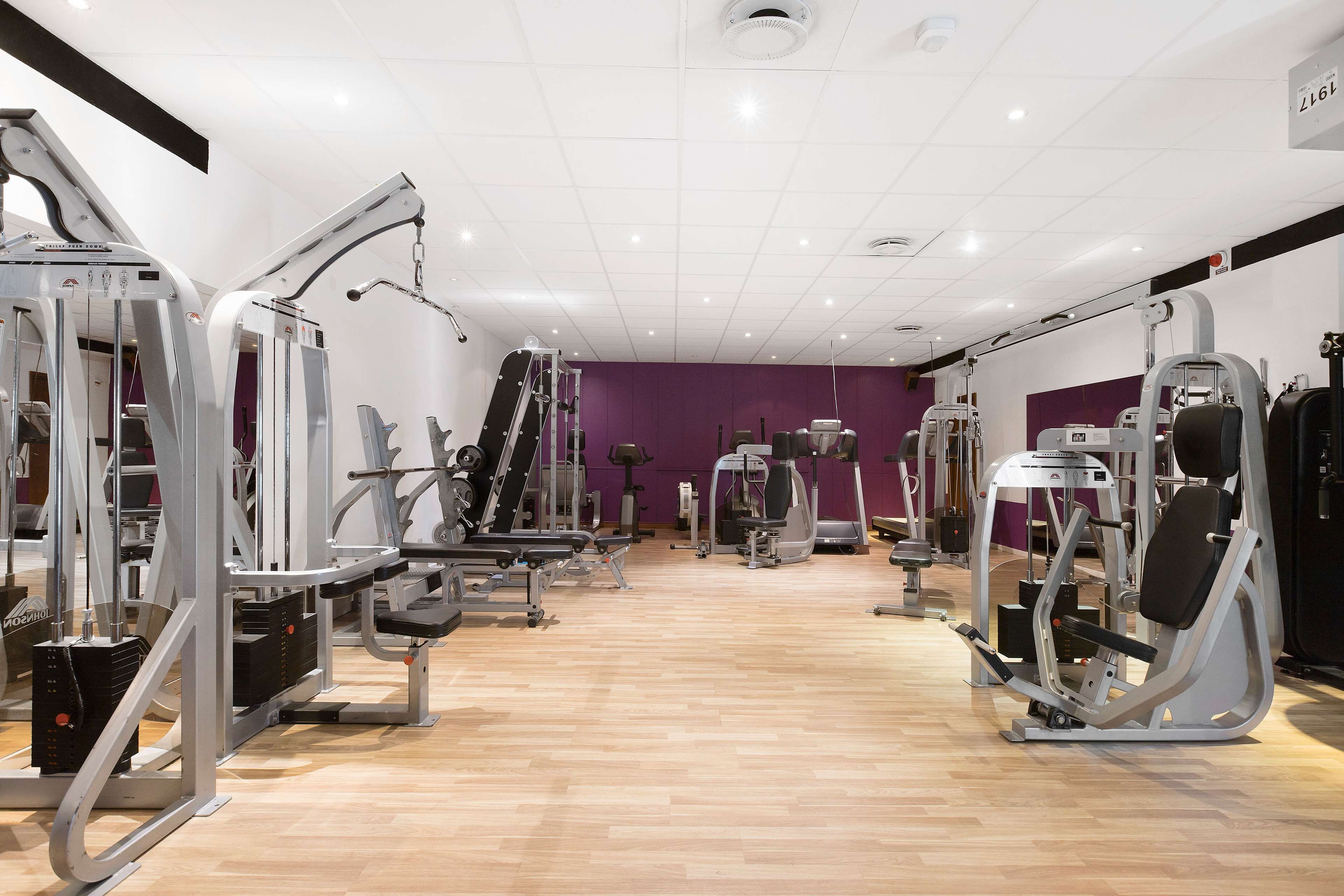 Ein Fitnessstudio mit verschiedenen Trainingsgeräten, einer violetten Wand und einem Holzboden.