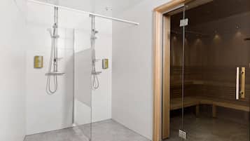 A modern bathroom with two glass-enclosed showers, a sauna, and a wooden bench.
