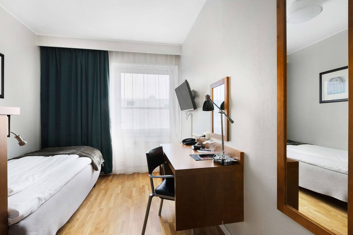 Een hotelkamer met een bed, een bureau, een stoel, een televisie en een raam met gordijnen.