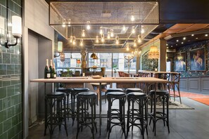 Zona de bar con varios taburetes, una barra larga y lámparas colgantes.