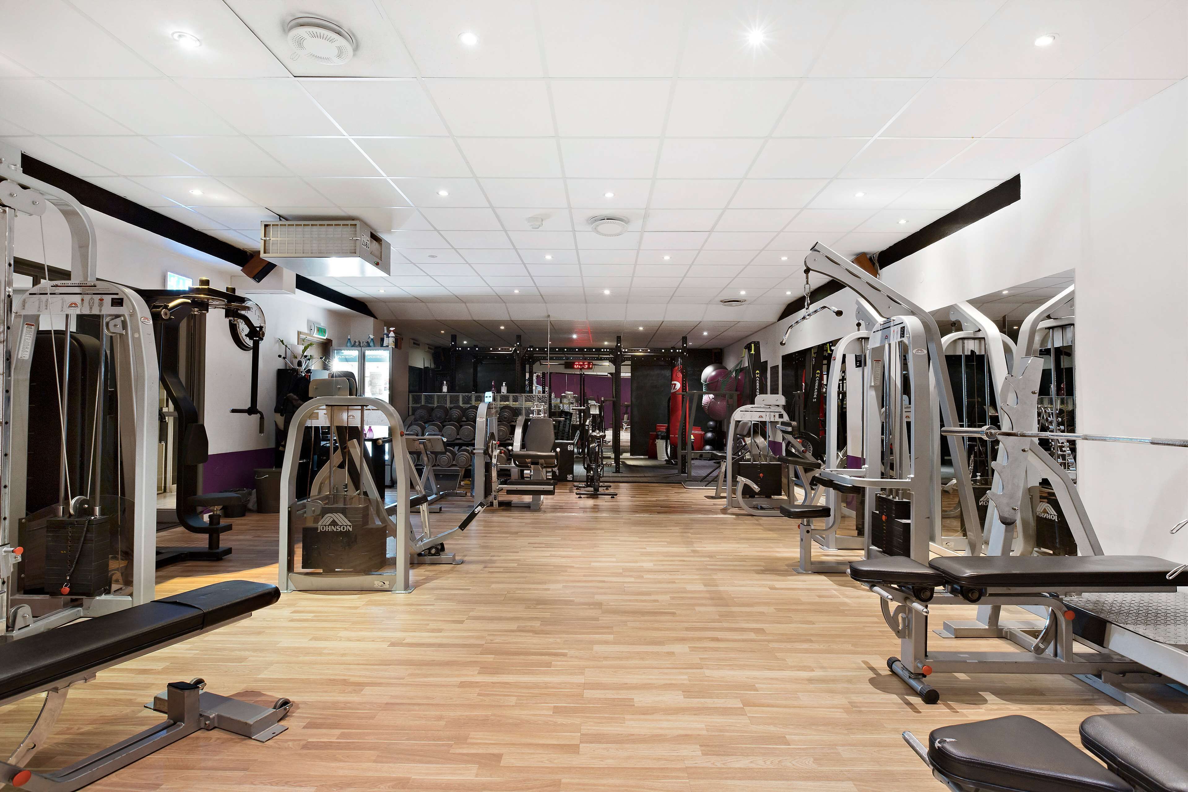 Un gimnasio con diversas máquinas de ejercicio, bancos y un espejo grande.
