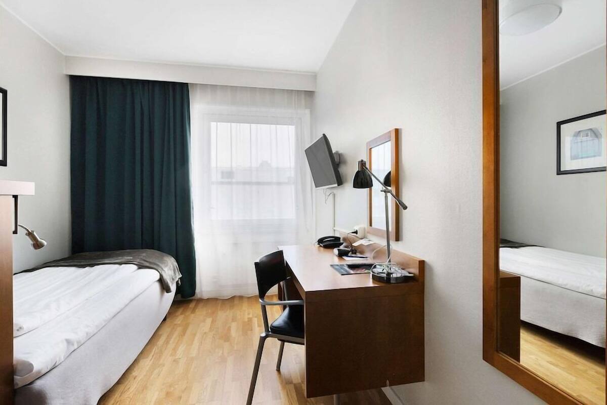 Een hotelkamer met een bed, een bureau, een stoel, een televisie en een raam met gordijnen.