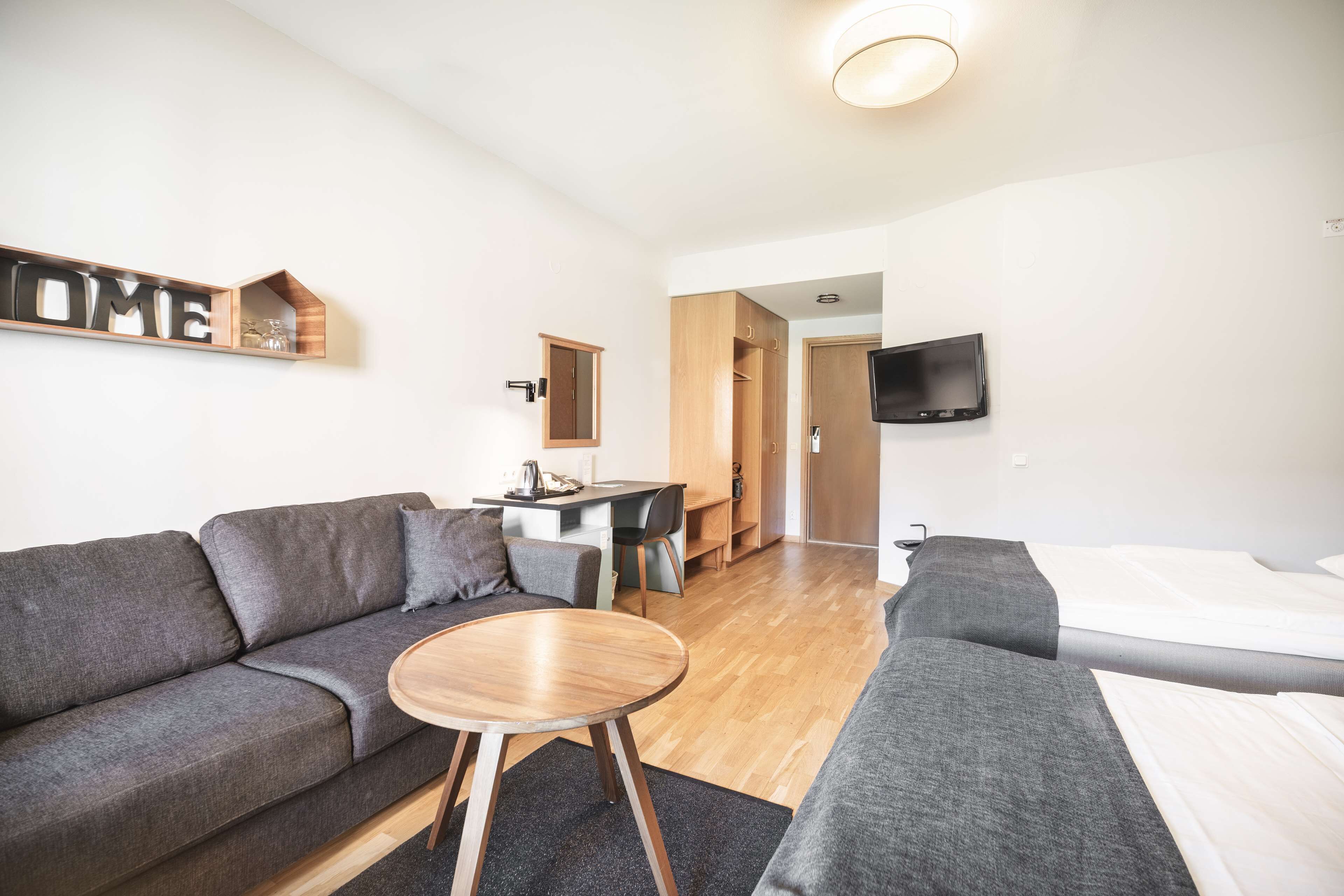 Ein modernes Wohnzimmer mit einer Couch, einem kleinen runden Tisch, einem an der Wand montierten Fernseher und einem Holzschrank.