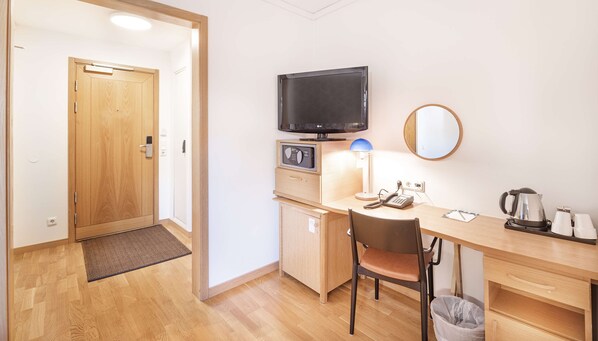 Habitación de hotel con puerta de madera, televisor, microondas, escritorio con silla, espejo y tetera.