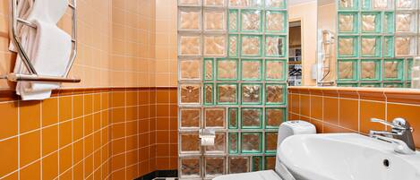 Un baño con suelo de baldosas, inodoro, lavabo y zona de ducha con paredes de vidrio.