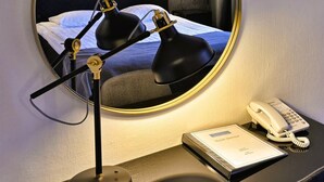 Habitación de hotel con un espejo redondo que refleja una cama, una lámpara de escritorio, un teléfono y un folleto de servicios.