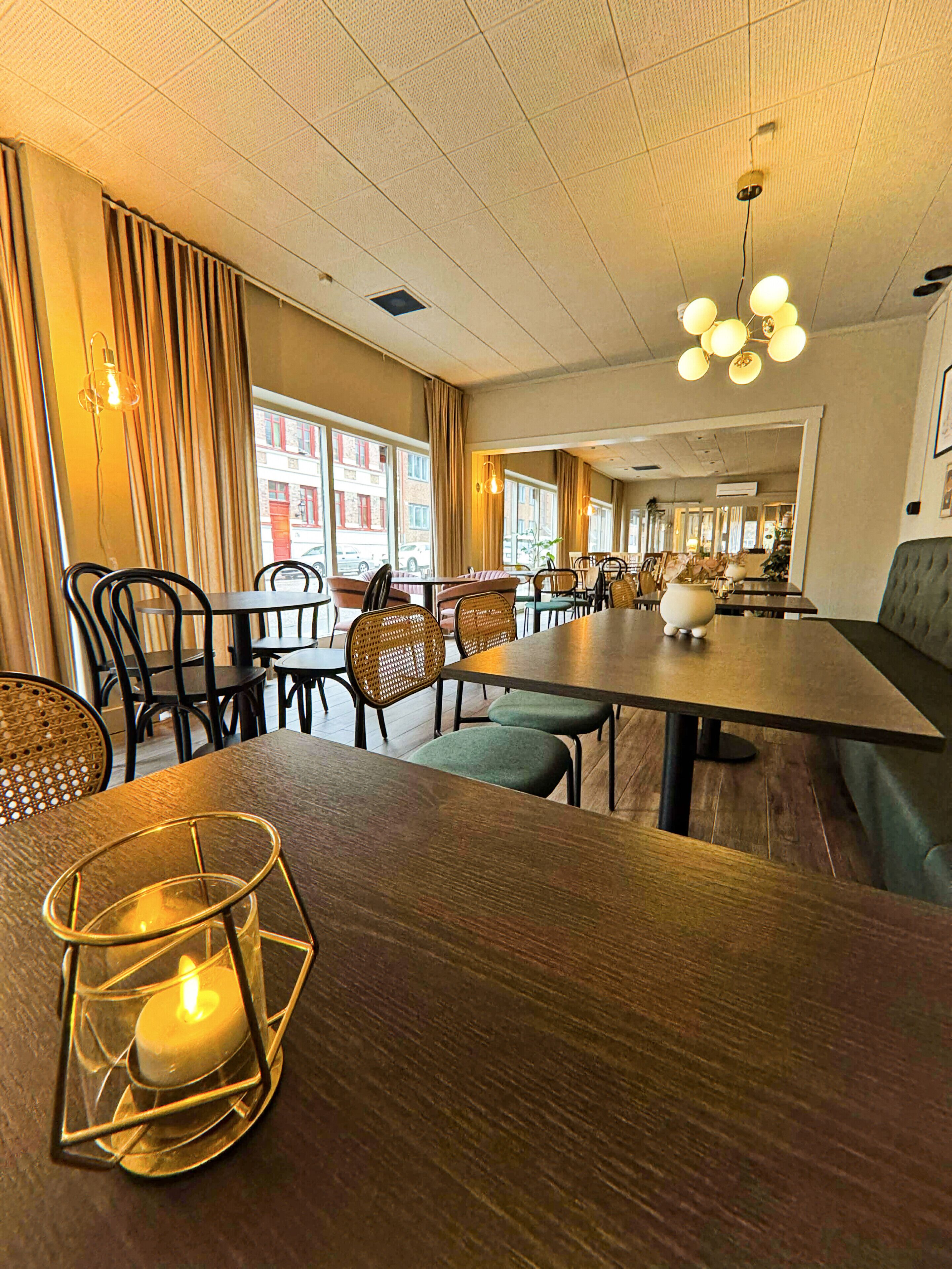 L’intérieur d’un restaurant avec des tables en bois, des chaises en osier et une bougie posée sur une table.