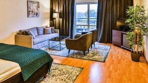 Una sala de estar acogedora con sofá, sillón, mesa de centro y televisor sobre piso de madera, con vista a un edificio.