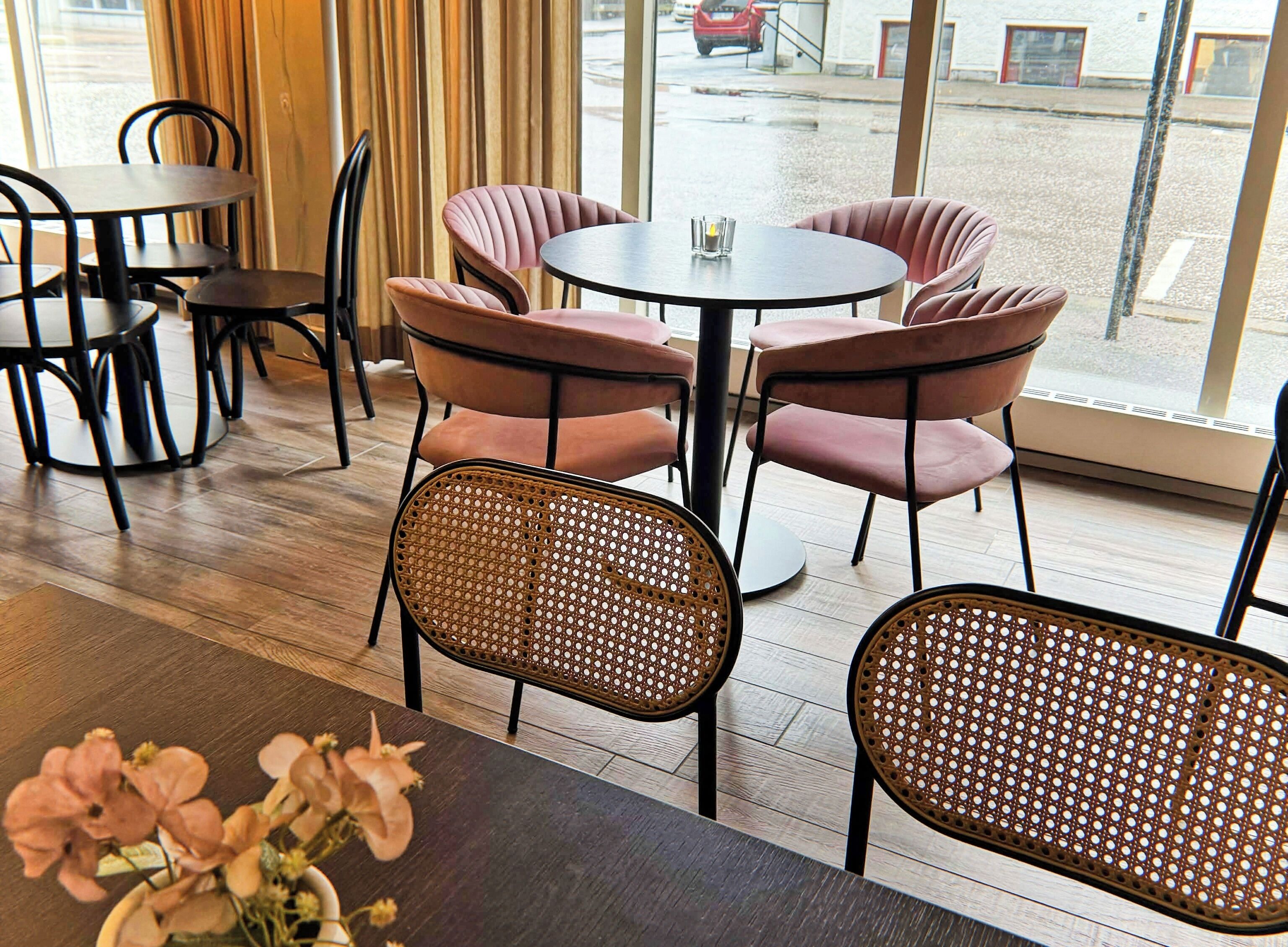A restaurant interior with round tables, cushioned chairs, and a view of the street through large windows.