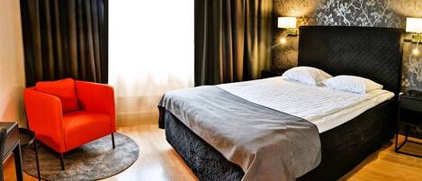 A hotel room with a large bed, a red armchair, and a round rug.