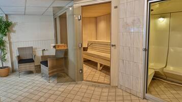 A sauna room with two wicker chairs, a wooden bench, and a glass door leading to a tiled area.