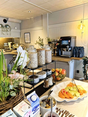 Un bufé de desayuno con diversos alimentos, una máquina de café y plantas decorativas.