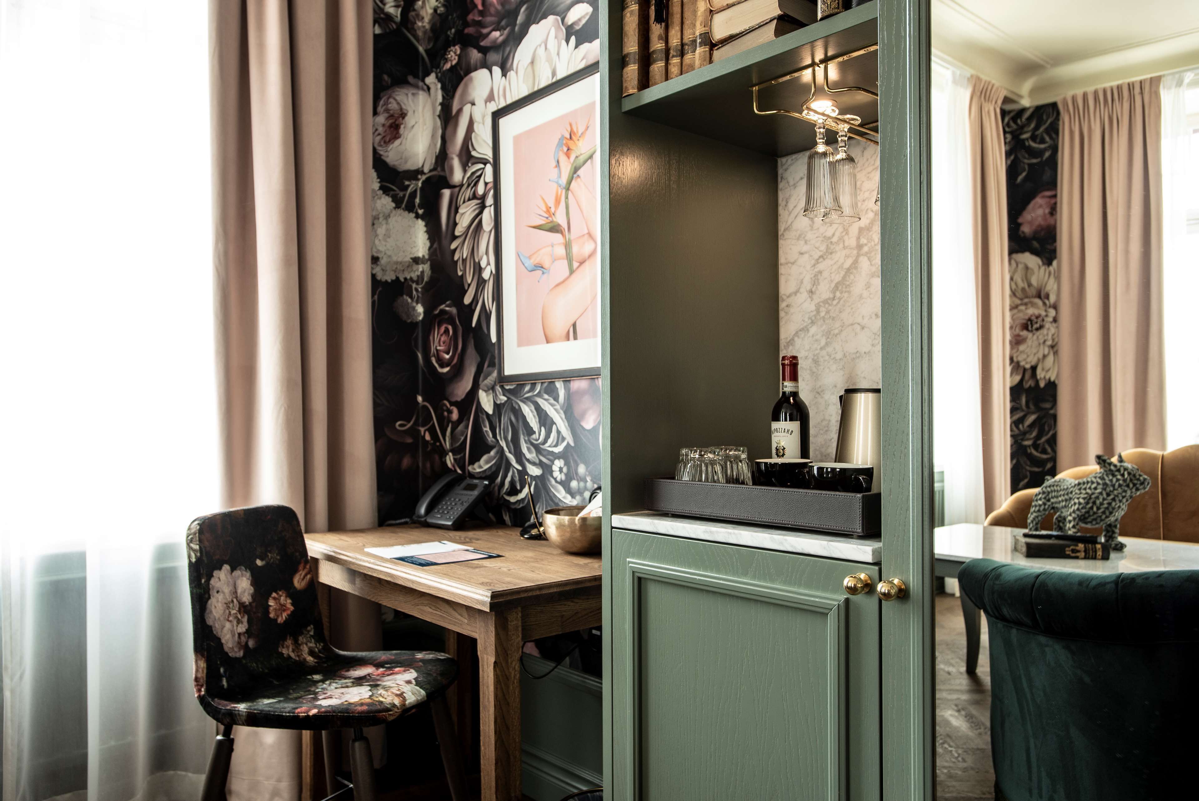 A room with a desk, chair, and a cabinet with a wine bottle and glasses.