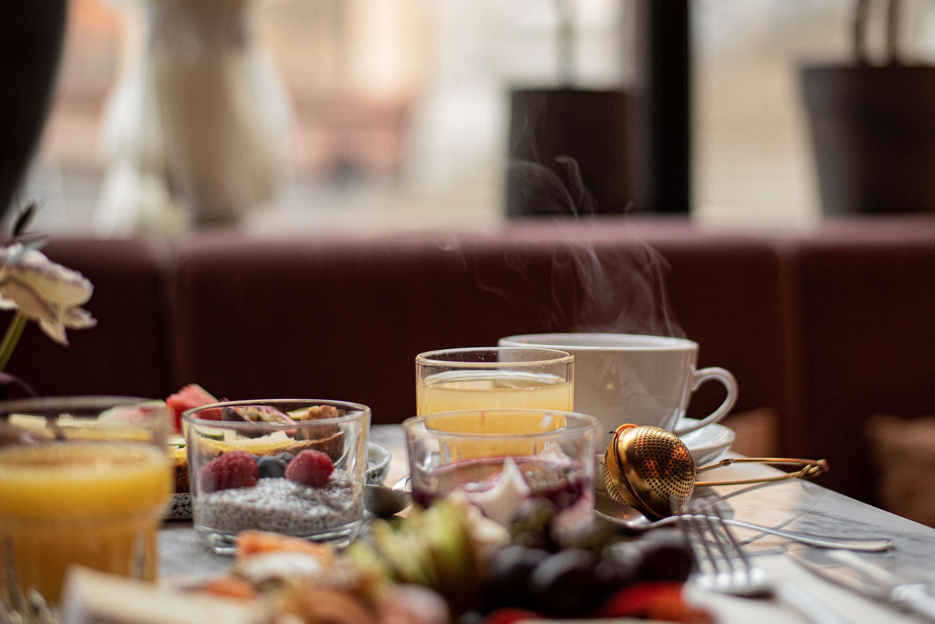 En frukostuppdukning med olika sorters mat och dryck, inklusive en kopp te, ett glas apelsinjuice och en skål med frukt.