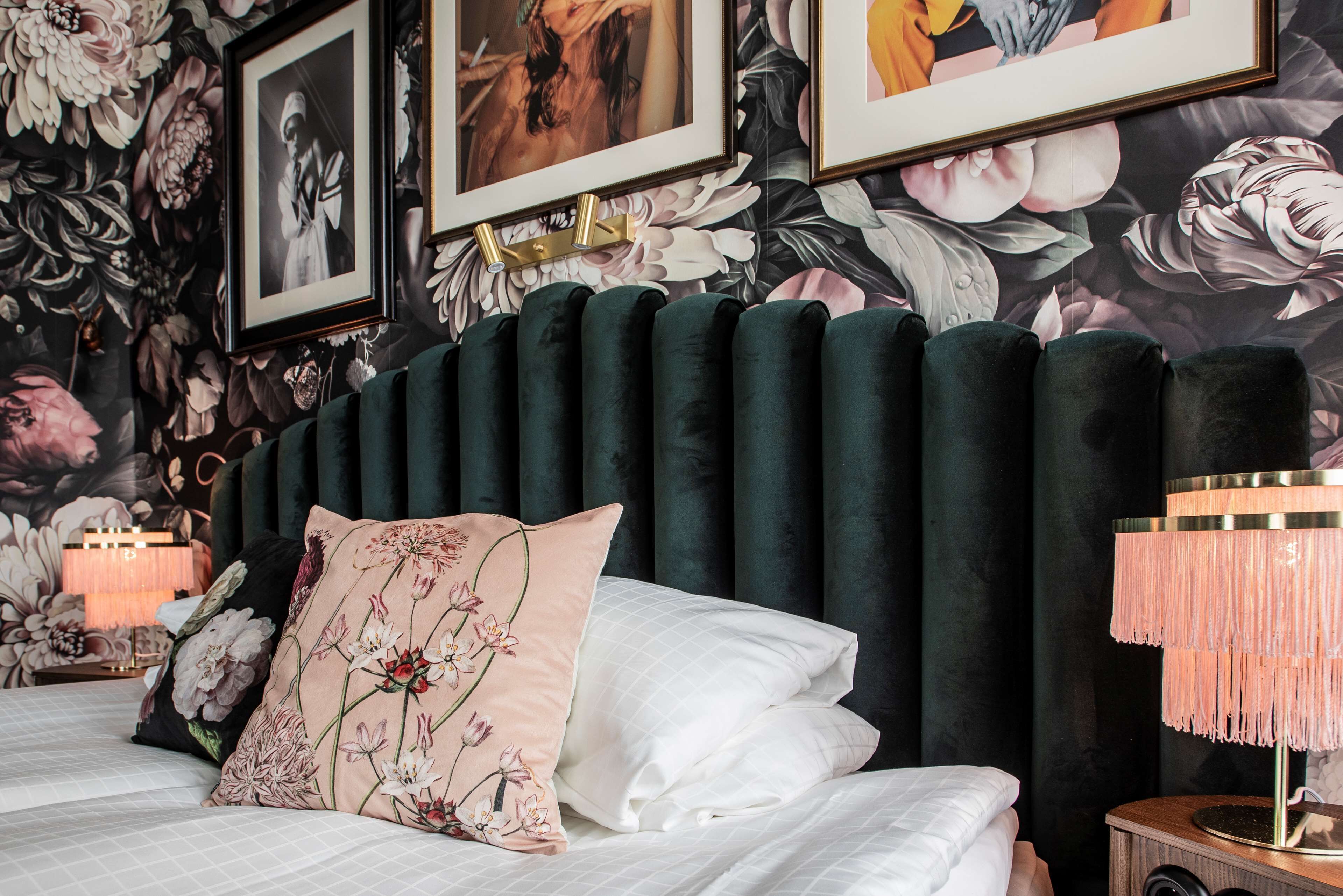A bed with floral-patterned pillows, a dark headboard, and a wall with large floral wallpaper.