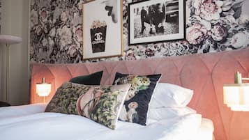 A neatly made bed with floral and Chanel-themed pillows, a tufted headboard, and framed pictures on the wall.