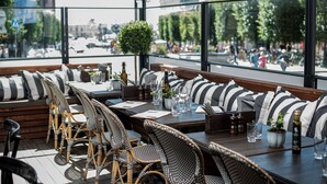 Un espace extérieur aménagé avec des chaises en osier et des coussins à rayures, une table en bois et une vue sur la rue.