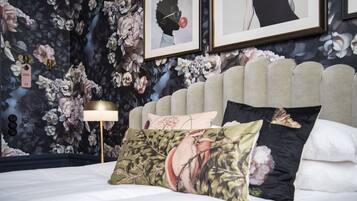 Un dormitorio con papel tapiz floral, un cabecero capitonado y una lámpara de noche.