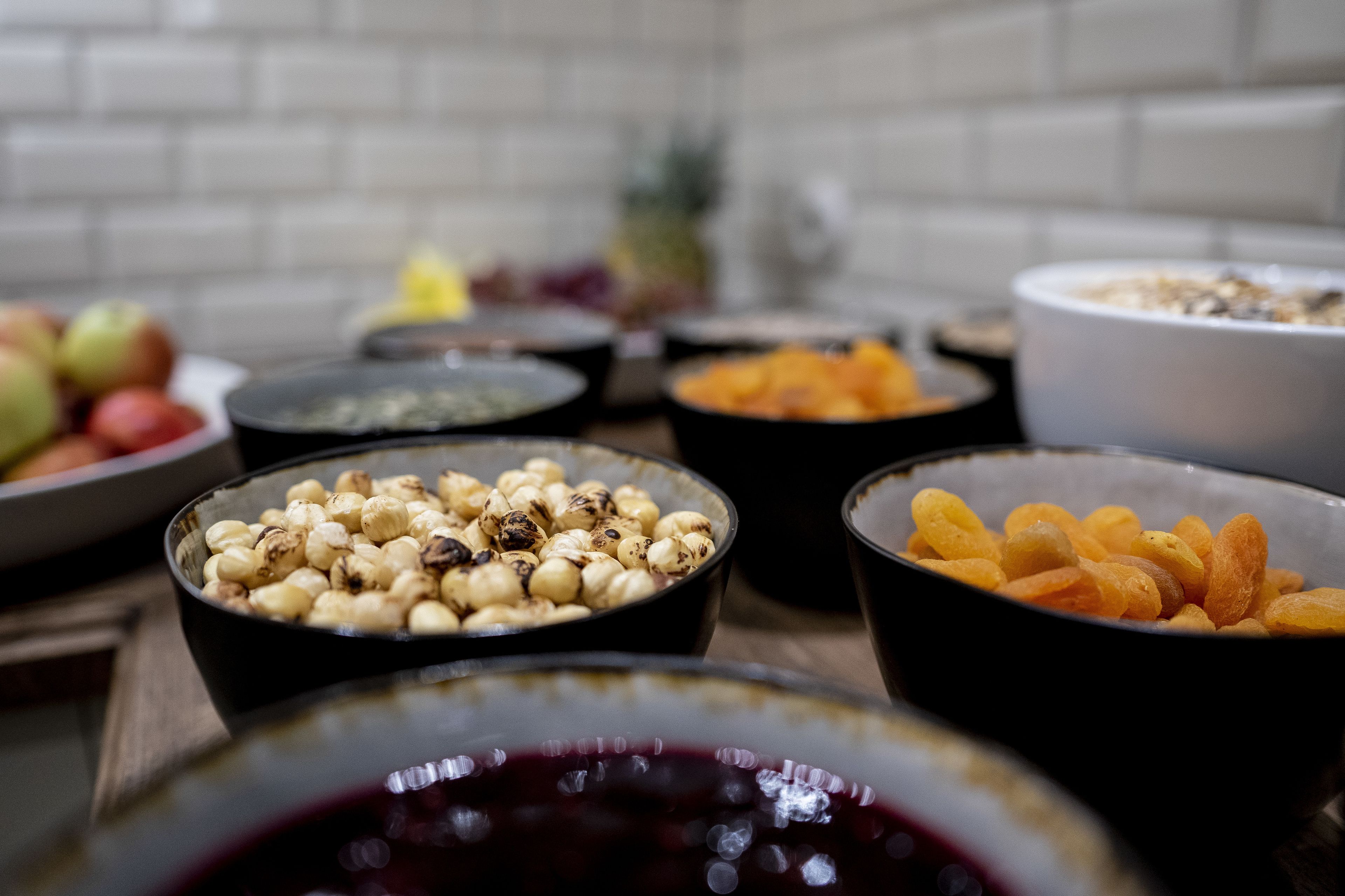 A variety of bowls containing different food items, including nuts, dried fruits, and a bowl of red fruit preserve.