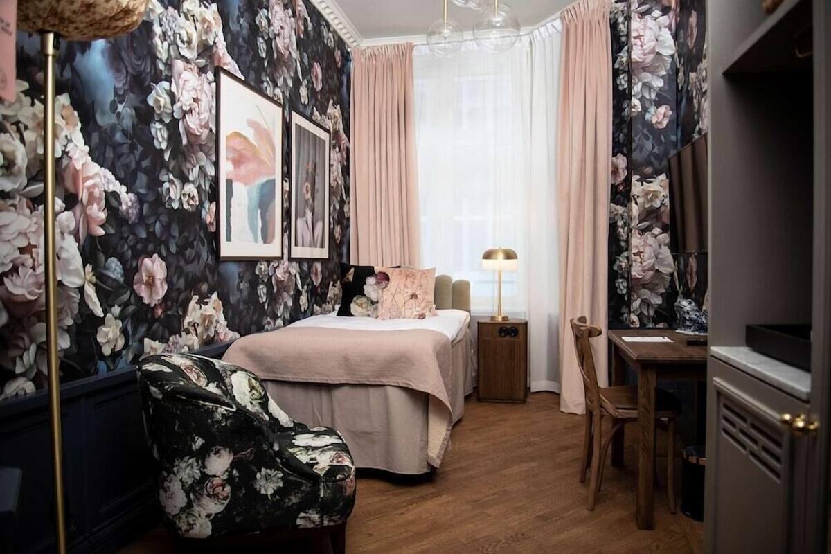 A bedroom with a bed, a desk, a chair, a lamp, and a window with curtains.