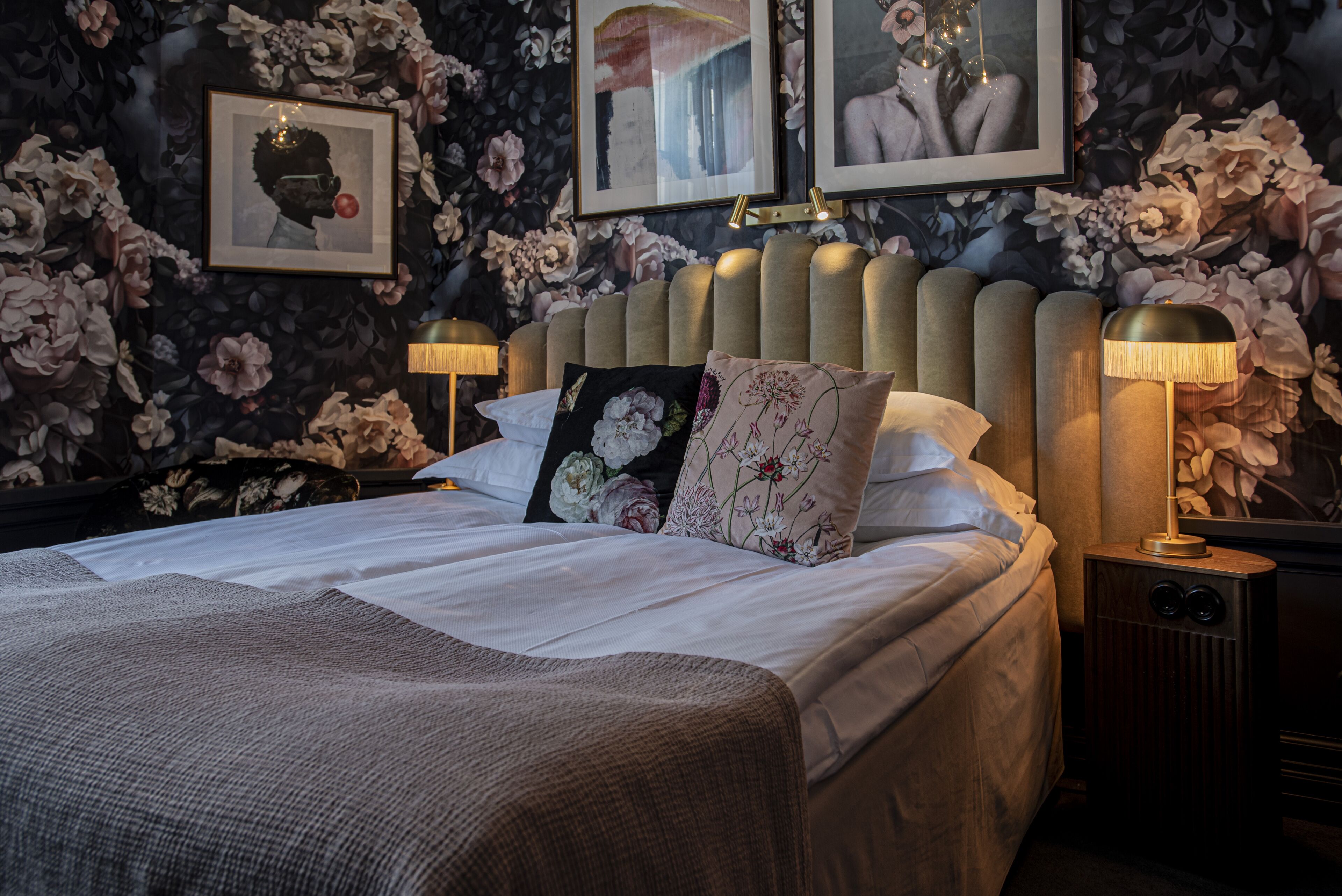 A neatly made bed with floral-patterned pillows and a headboard, flanked by two bedside lamps.