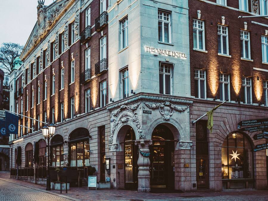 En historisk bygning med skiltet "The Vault Hotel", præget af udsmykket arkitektur og en veloplyst facade.