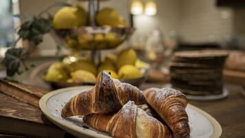 A plate with croissants on a wooden table, a bowl of lemons, and a stack of bread rolls in the background.