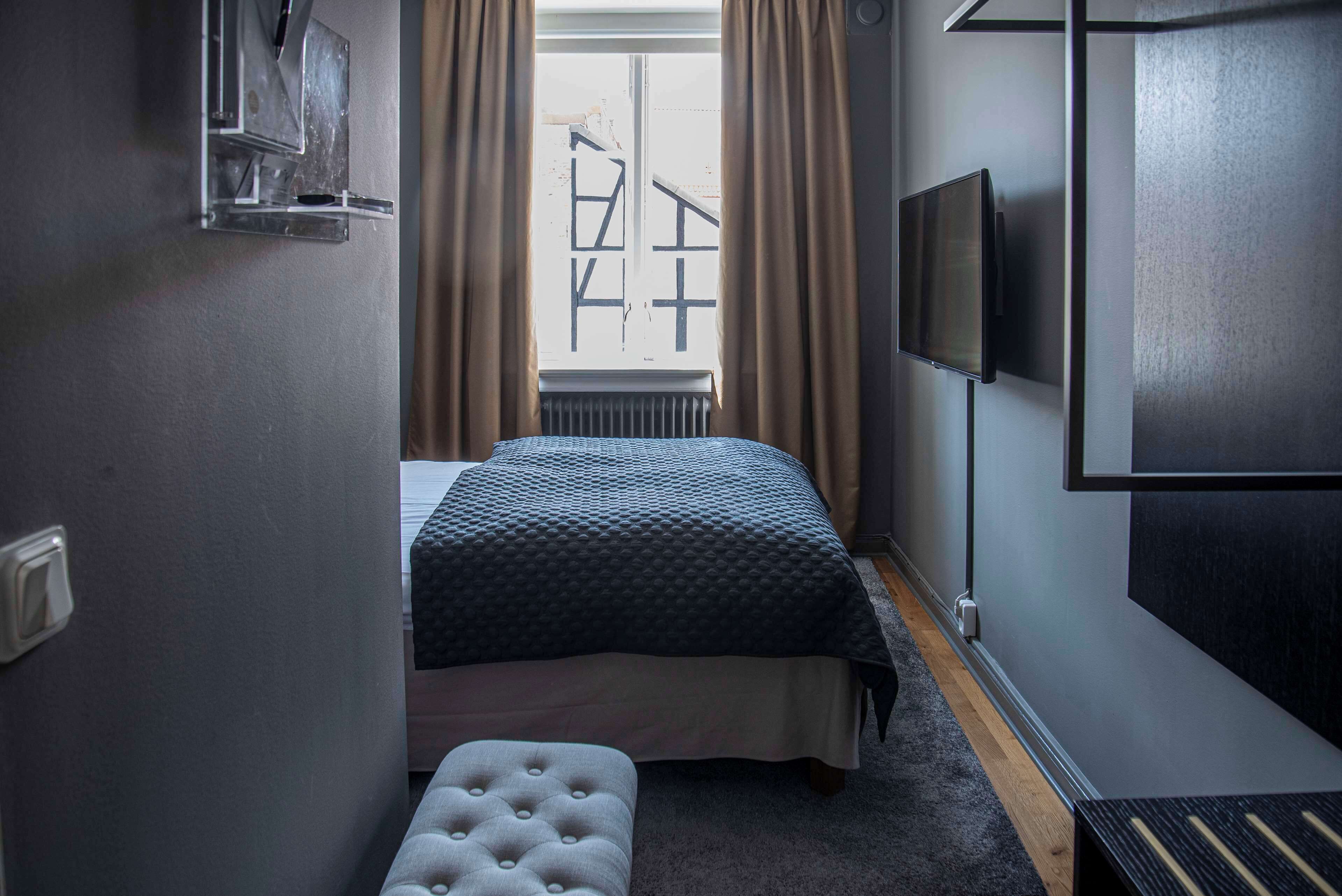 Un dormitorio con cama, televisor, ventana con cortinas y radiador.