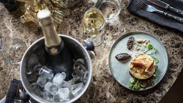 A dining table with a bottle of champagne, a glass of wine, and a plate of food.