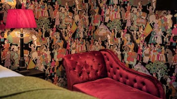 A room with a red upholstered sofa, a lamp, and a wall covered with colorful artwork.