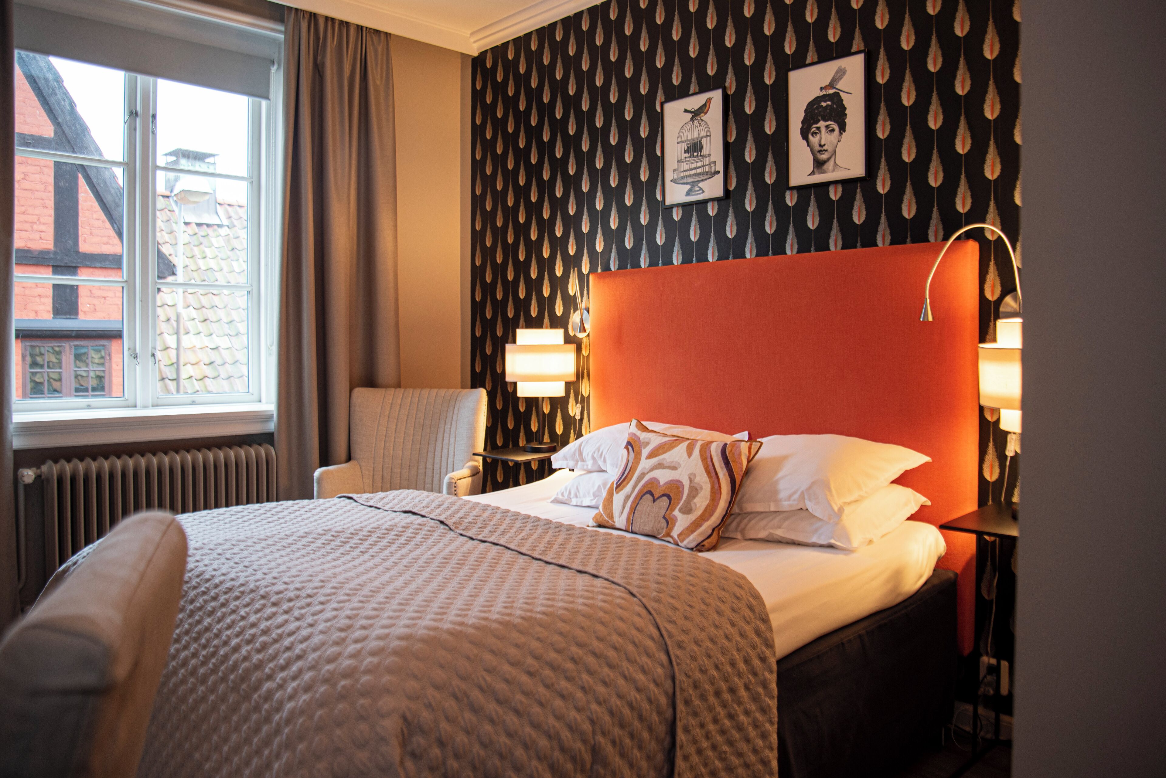 A hotel room with a large bed, two bedside lamps, a chair, and a window with a view of a building.