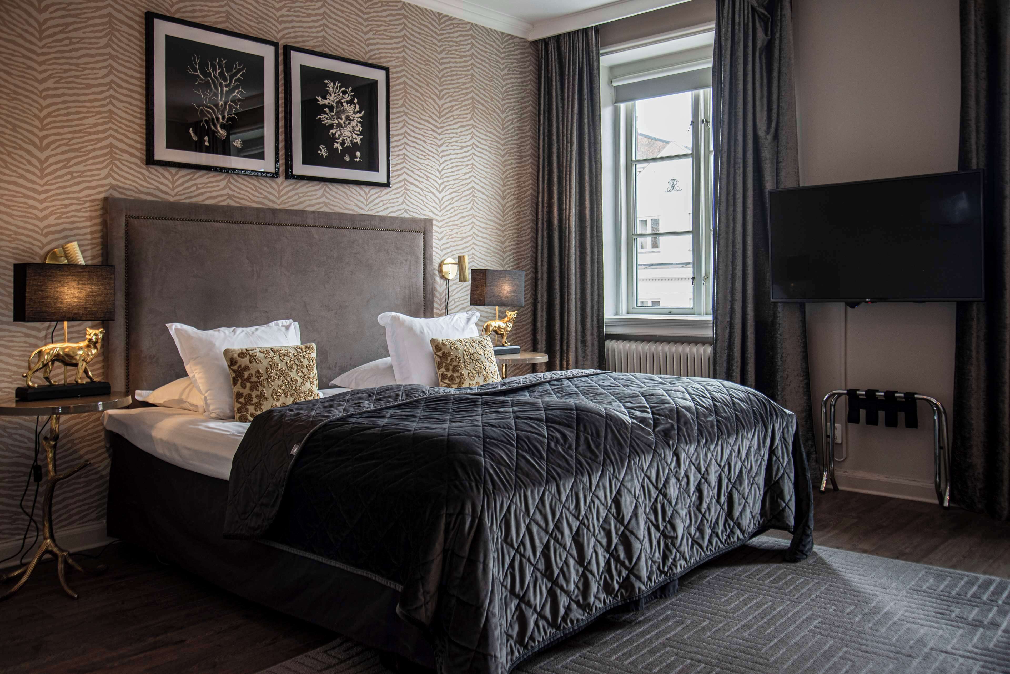 Une chambre d’hôtel avec un grand lit, deux tables de chevet avec des lampes, un téléviseur à écran plat, un radiateur et une fenêtre avec des rideaux.