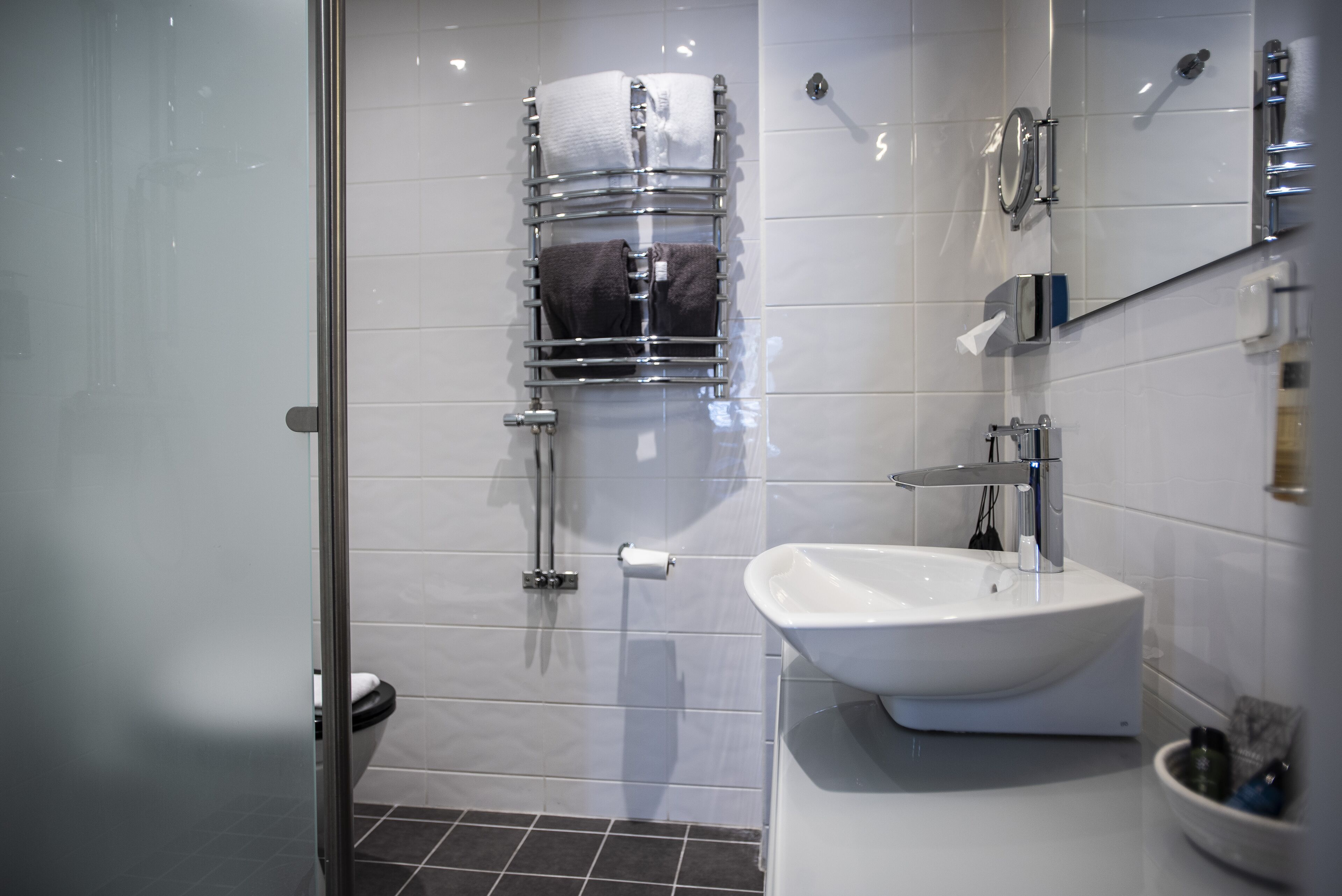 Un baño moderno con cabina de ducha de vidrio, un lavabo blanco y un perchero con toallas.