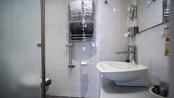 Un baño moderno con cabina de ducha de vidrio, un lavabo blanco y un perchero con toallas.
