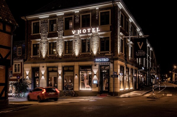 Un hotel con un bistró, que presenta una fachada clásica con señalización iluminada y una bicicleta estacionada afuera.