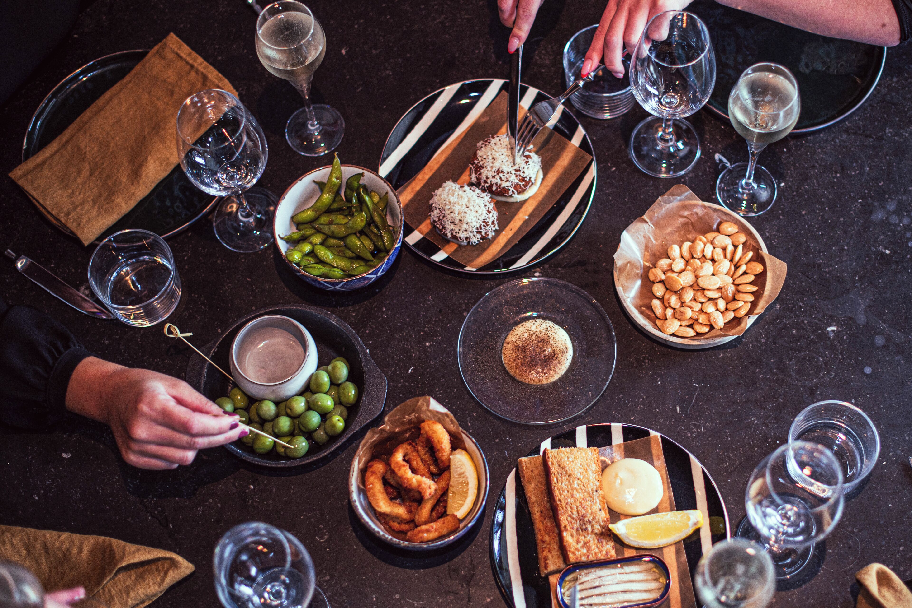 A table set with various dishes and drinks, including olives, bread, and a bowl of almonds.