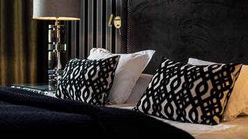 Una cama bien hecha con almohadones estampados, una lámpara de noche y un cabecero oscuro.