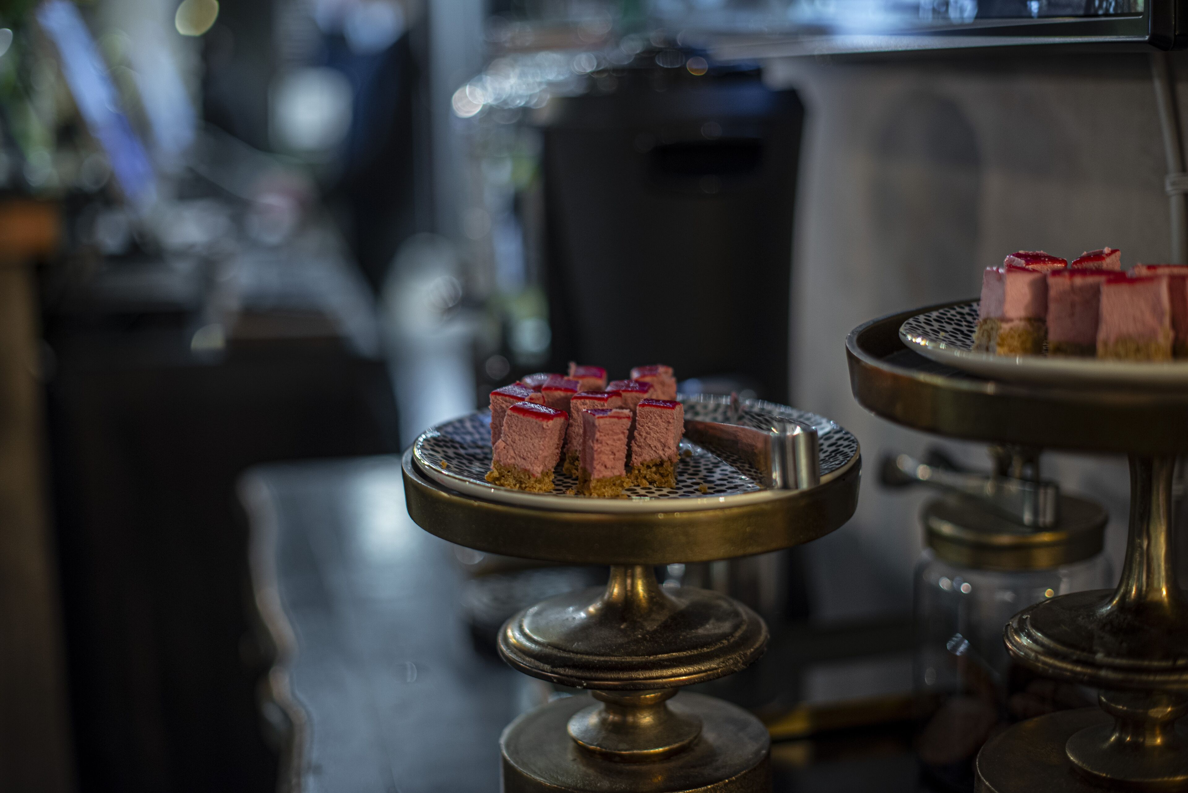 A dessert display with multiple trays of pink and red desserts on a bar counter.