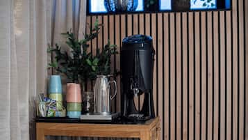 Une machine à café posée sur une table en bois, avec des tasses empilées et un pichet à côté.