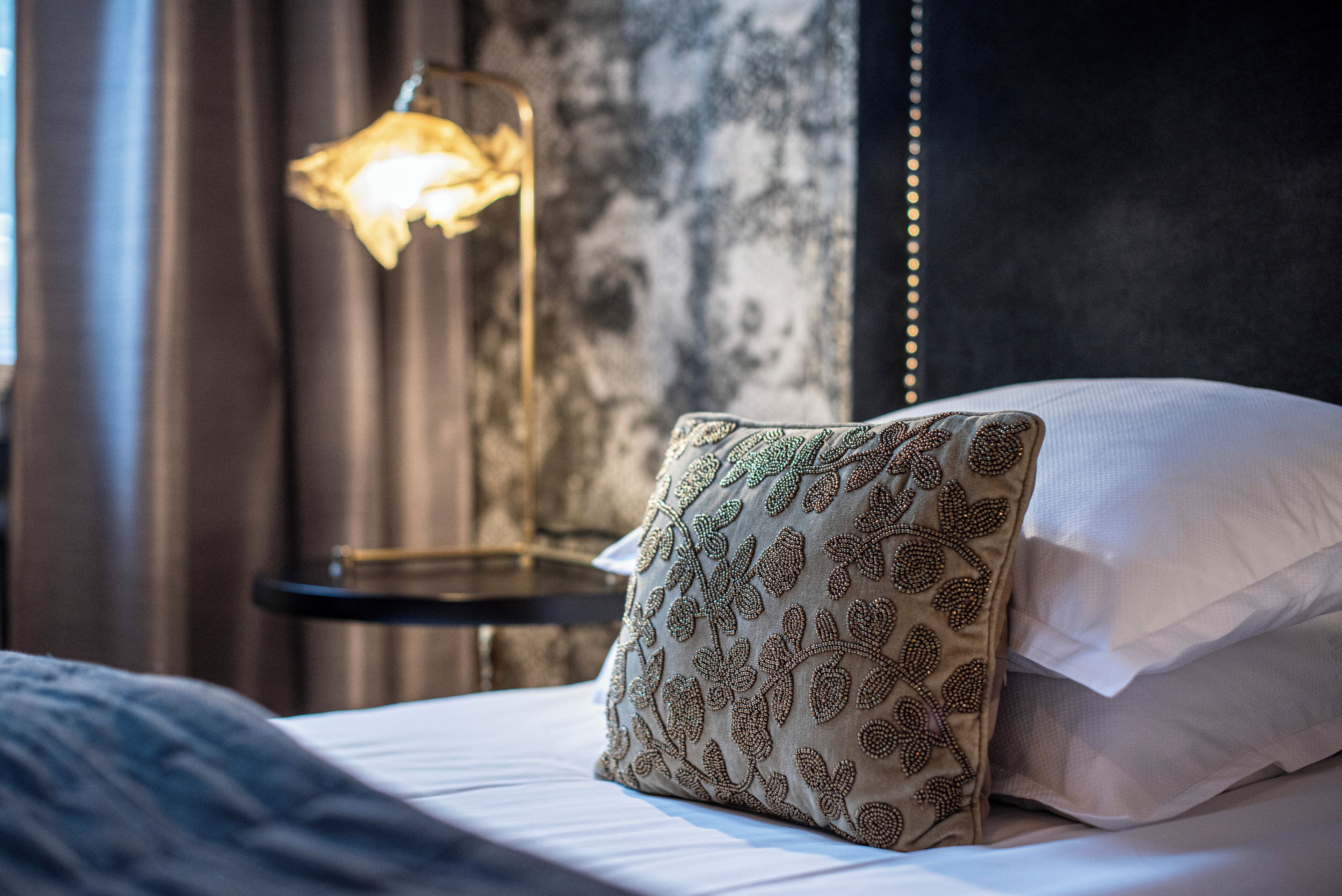 A neatly made bed with a patterned pillow and a bedside lamp.