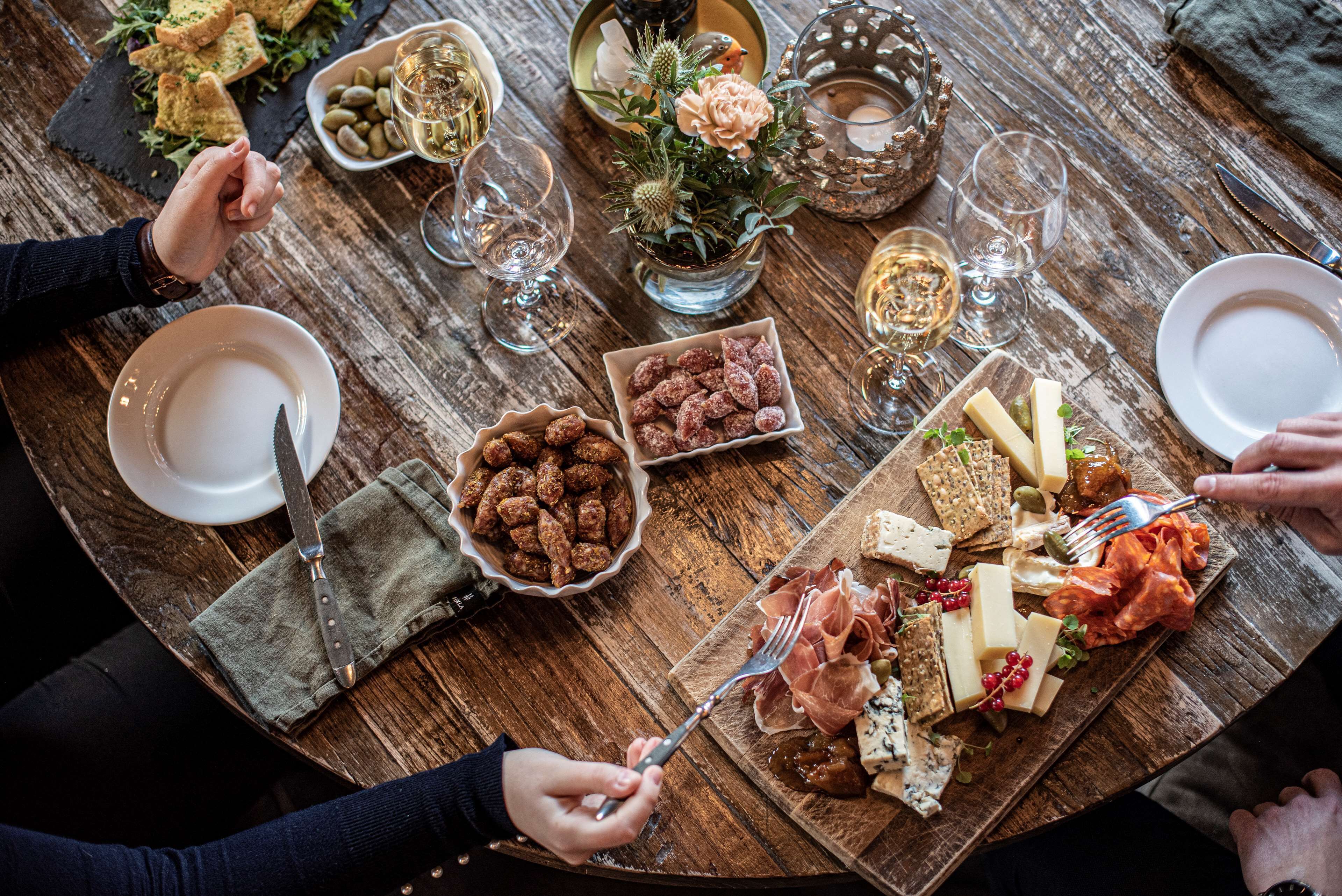 Una mesa de madera con diversos alimentos, copas de vino y un centro de mesa con flores.