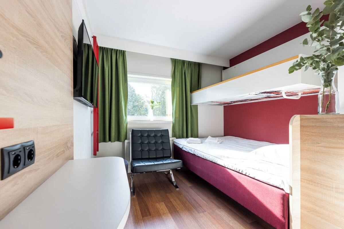 A compact room with a bunk bed, a small desk, a chair, and a window with curtains.