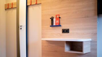 A hotel room with a wooden wall, a white shelf, a door, and a red sign.