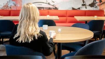 Een persoon zit aan een ronde tafel in een café met rode stoelen en een muurschildering op de achtergrond.