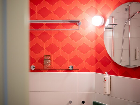 Un baño con pared de diseño rojo, un frasco de vidrio en una repisa, una botella blanca y un espejo.